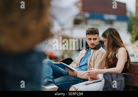 Two students studying and talking together on a bench in an outdoor urban setting Stock Photo