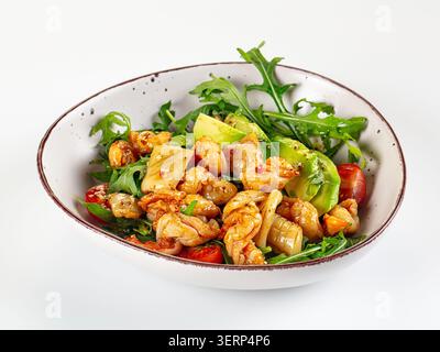 Fresh seafood salad featuring grilled shrimp squid avocado slices cherry tomatoes and arugula leaves served in rustic ceramic bowl isolated on white b Stock Photo