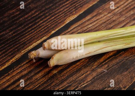 Three fresh lemongrass stalks diagonally arranged on dark rustic wooden background. Natural light highlights green pale yellow colors, earthy texture Stock Photo
