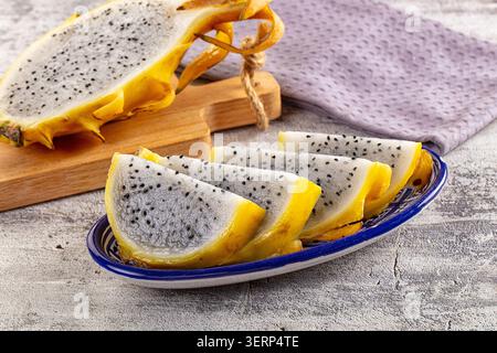 Fresh yellow dragon fruit, known as pitaya, presented as whole half fruit elegant slices on decorative blue plate Stock Photo
