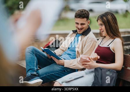 Two students laughing and studying together on a park bench with books and phone Stock Photo
