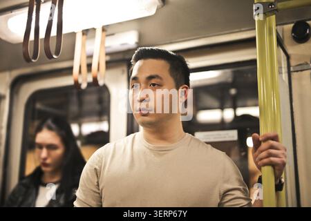 Young Asian man holding a pole on public transportation Stock Photo