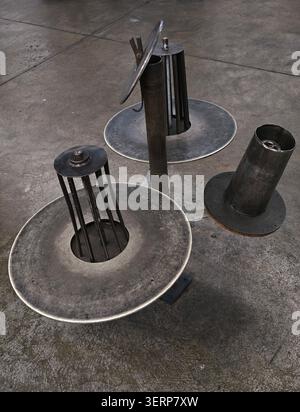 Group of three weathered metal vent and duct components arranged on stained concrete workshop floor, showing circular plates, cylindrical chimneys Stock Photo