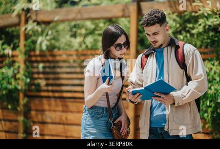 Two students studying and discussing notes together outdoors by a wooden fence Stock Photo
