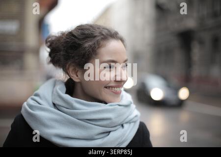 Happy young woman with a blue scarf smiling in the city Stock Photo