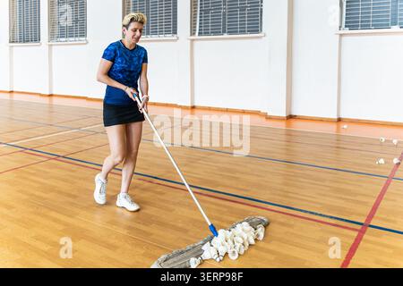Female athlete sweeping up shuttlecocks with a mop Stock Photo