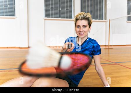 Female badminton player smiles sitting on gym floor Stock Photo