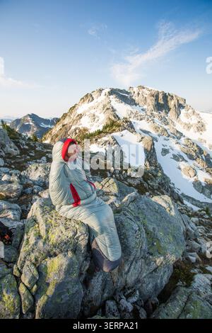 Hiker sitting in a sleeping bag on a mountain peak Stock Photo