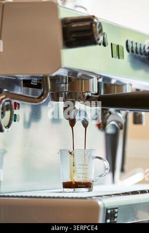Espresso being extracted from a professional coffee machine into glass cups, close up view of coffee brewing process in a cafe Stock Photo