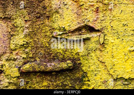 Corroding industrial metal surface featuring a textured background with vibrant yellow peeling paint and visible rust, forming an abstract pattern fro Stock Photo