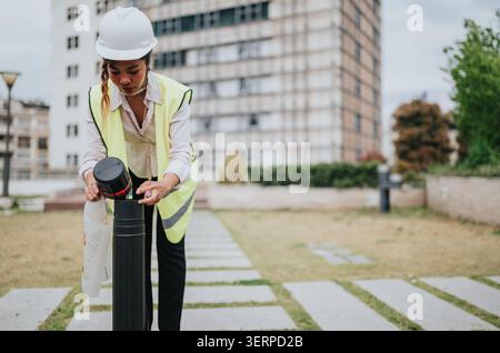 Female construction engineer in hard hat and safety vest checking blueprints on an urban building site Stock Photo