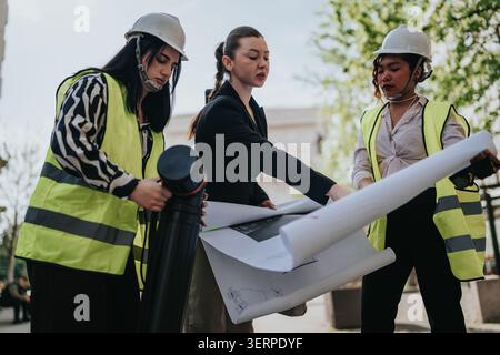 Women architects and engineers reviewing blueprints on a construction site during a planning meeting Stock Photo