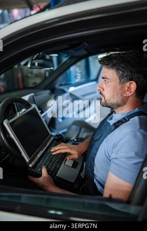 Car mechanic using diagnostic software on a laptop inside a vehicle Stock Photo