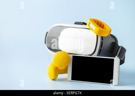 Composition of gadgets for tracking healthy training on blue background. Set of VR headset with smartwatch and mobile phone with yellow dumbbells. Stock Photo