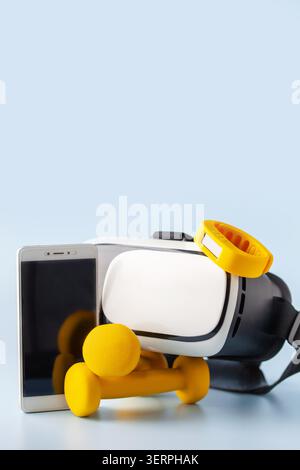 Composition of gadgets for tracking healthy training on blue background. Set of VR headset with smartwatch and mobile phone with yellow dumbbells. Stock Photo