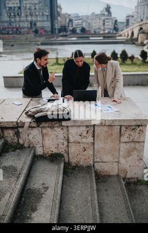 Winter outdoor business meeting with colleagues collaborating over laptop and documents by riverside Stock Photo