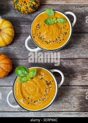 Creamy pumpkin soup served in white bowls with basil leaves and seeds on a rustic wooden table Stock Photo
