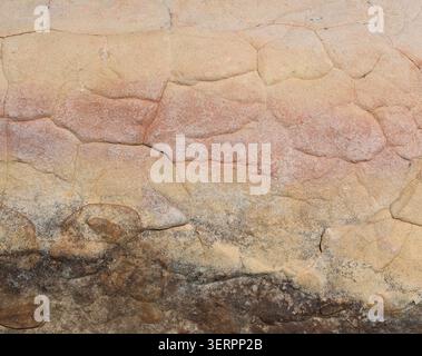 Close up of a large weathered stone surface with uneven cracks, light pinkish tan color at the top, light to medium brown at the bottom Stock Photo