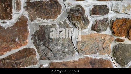 Close up of a rock and mortar wall surface with thick uneven mortar joints, large vertical crack, varied stones in multiple sizes, shapes, and colors Stock Photo