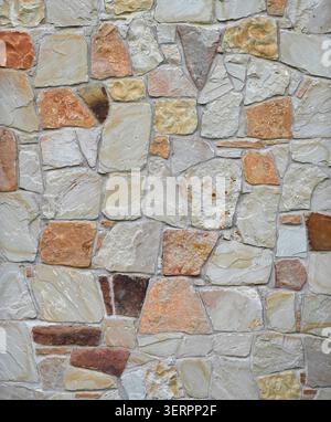 Close up of a rock wall and mortar surface with flat uneven stones in varied sizes, shapes, and gray to brown colors Stock Photo