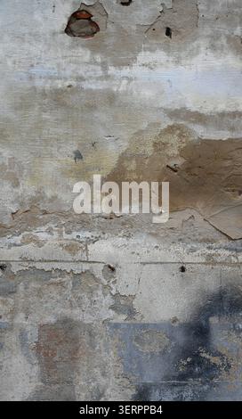 Weathered deteriorating concrete wall surface with multiple cement layers, worn paint, exposed red brick areas, terra cotta patch Stock Photo