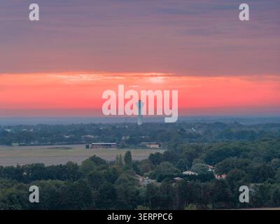 Silhouetted against a pink and orange sky over fields, trees and scattered houses, Mache, France Stock Photo
