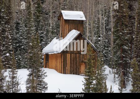 Aerial view of a historic wooden mine building covered in deep snow surrounded by a dense forest of pine and aspen trees along the Million Dollar High Stock Photo