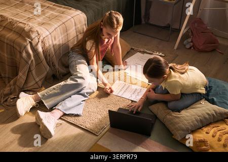 Two girls studying music, reading sheet notes, using laptop, practicing instrument lessons at home. Education and creative learning concept for homeschooling, music school promotion Stock Photo