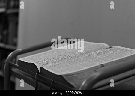 Open dictionary resting on a reading stand in a quiet indoor study setting, showing printed definitions and supporting language learning and reference Stock Photo