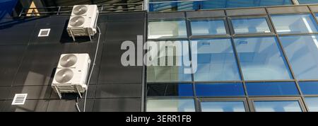 Two external wall mounted air conditioners cool modern homes and offices, providing comfort and climate control. Glass windows. Bottom view. Stock Photo