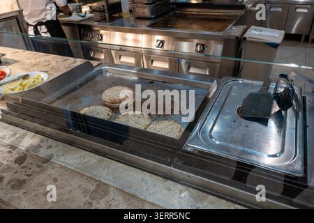 Flat round pita breads being warmed up on a large commercial electric flat top griddle station. Located at a restaurant buffet or live cooking hotel s Stock Photo