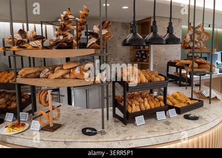 A large display of freshly baked artisan bread, buns, croissants, and traditional pastries arranged on wooden shelves and stands. This hotel buffet or Stock Photo