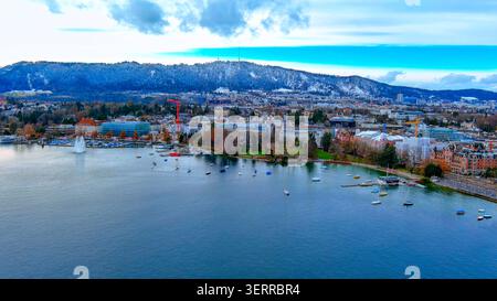 Aerial drone view of Lake Zurich waterfront with sailboats, lakefront fountain, city and snow-covered Zürichberg, Switzerland Stock Photo