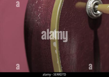 Close-up view of vintage red decorative instrument part, featuring cracked paint and wear marks, highlighting smooth yellow edge trim and metallic kno Stock Photo