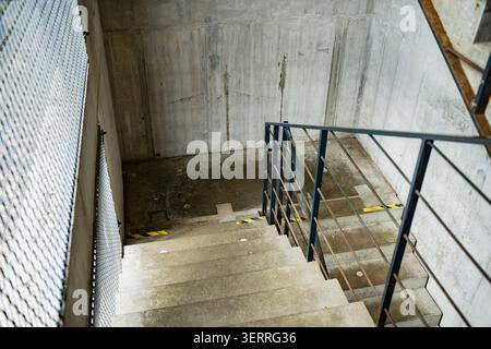 Industrial minimalist concrete staircase leading down to a landing area with steel mesh panels and architectural safety features outdoors Stock Photo