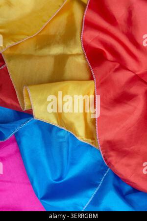 Bright colorful fabric folds in red, yellow, blue, and pink, suitable for textile background, creative design, and abstract texture concept. Stock Photo