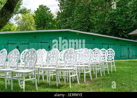 White decorative chairs in front of green boathouse waiting for wedding guests Stock Photo