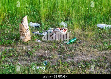 Abandoned trash from a picnic left in a green grassy field, consisting of empty plastic bottles, paper bags and litter scattered on the ground: Russia Stock Photo