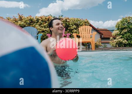 Young man playing with a bright ball in a backyard swimming pool on a sunny day Stock Photo