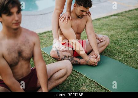 Two men practicing partner yoga and stretching on mats by a poolside lawn Stock Photo