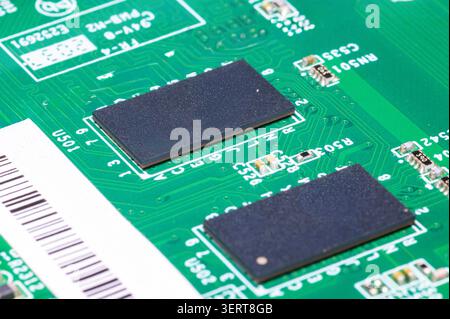 Green circuit board featuring black rectangular microchips, tiny resistors, and printed electronic pathways. Stock Photo