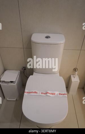 High-angle shot of a clean white ceramic toilet bowl with a red and white paper strip indicating it has been disinfected. Stock Photo