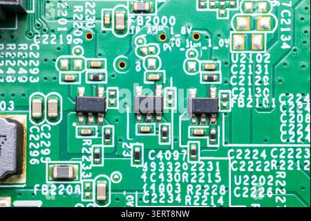 Green circuit board surface with black integrated circuits and numerous tiny electronic components. Stock Photo