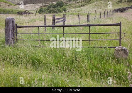 An old metal farm gate and concrete post in a grassy field with a vintage stone waterworks boundary marker at Dovestone Reservoir, UK. Stock Photo