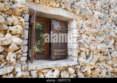 Charming rustic window with dark wooden shutters on a weathered stone wall. Perfect for Mediterranean lifestyle, authentic architectural textures. Stock Photo