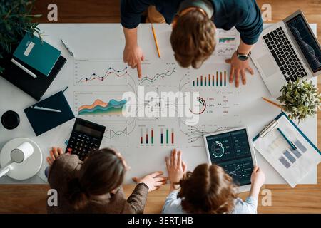 Dynamic overhead shot of a collaborative team meeting in a contemporary workspace, focusing on business analytics, financial graphs, and artificial in Stock Photo