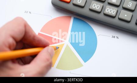 A businessman analyzing a colorful financial pie chart on a printed document using a pen and a calculator. Close up. Stock Photo