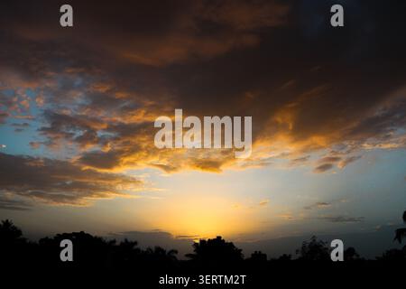 Golden sunset sky with dramatic glowing clouds above dark silhouettes. A breathtaking sunset landscape featuring dramatic orange. Stock Photo