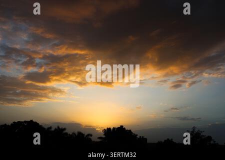 Fiery evening clouds painting the sky at dusk. Beautiful dusk scenery with fiery clouds illuminated by the setting sun. The mix of warm golden tones. Stock Photo