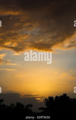 Colorful twilight sky over peaceful countryside horizon. A serene twilight sky filled with textured clouds glowing in shades of orange, yellow. Stock Photo